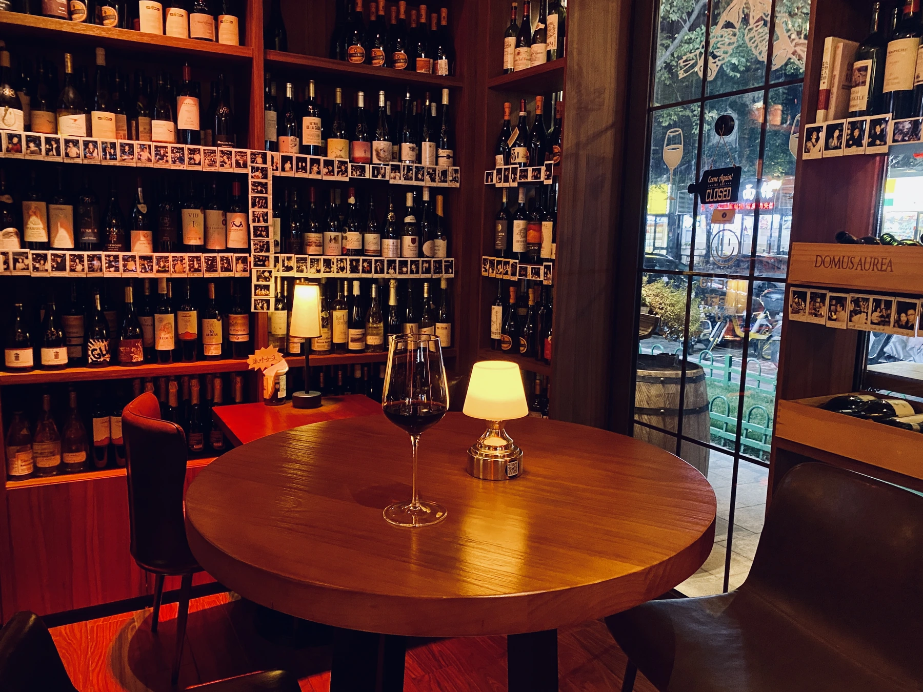 A glass of wine at a table beside the wine shelves