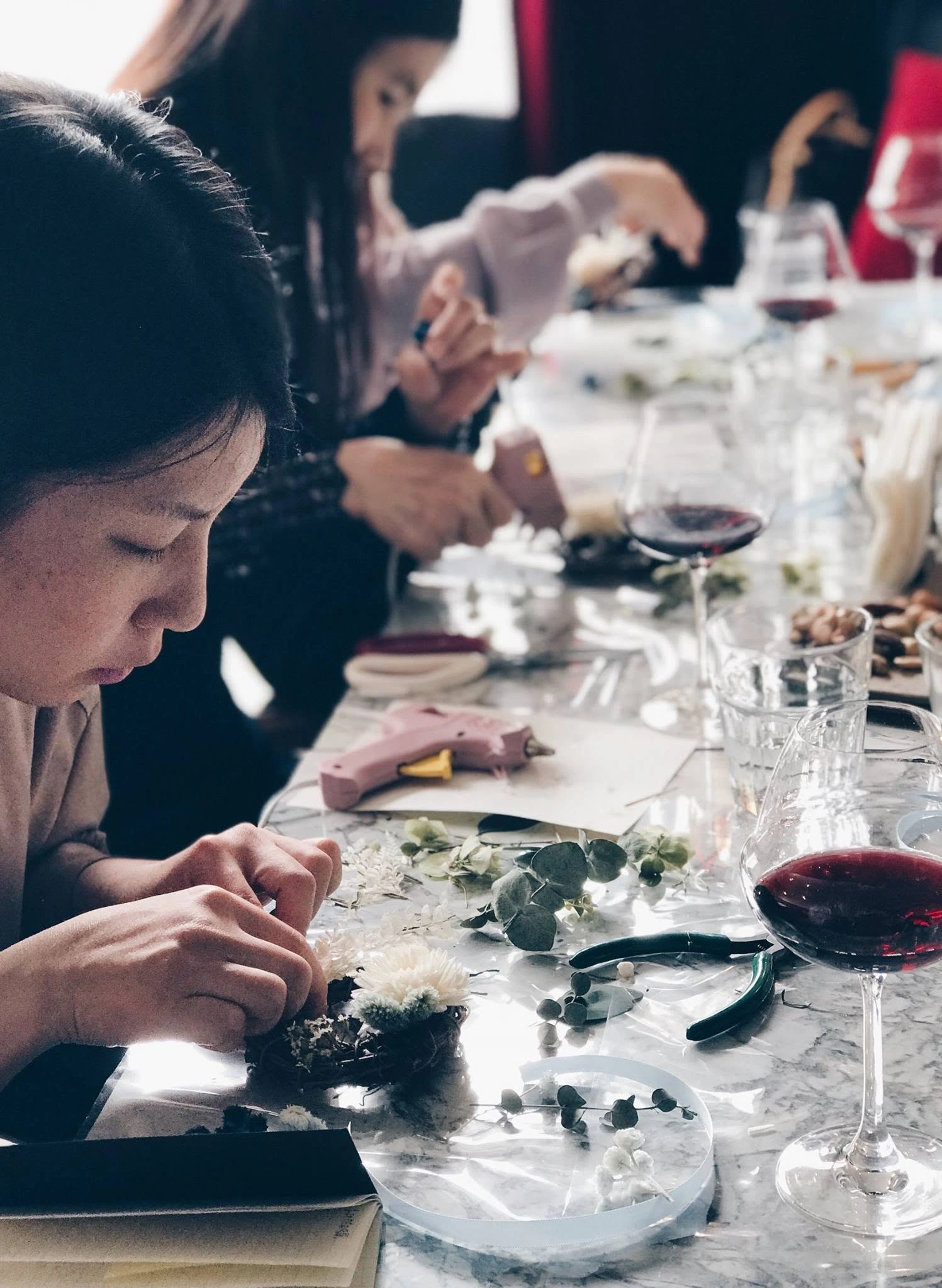Hands arranging flowers beside wine glasses at a shared creative workshop