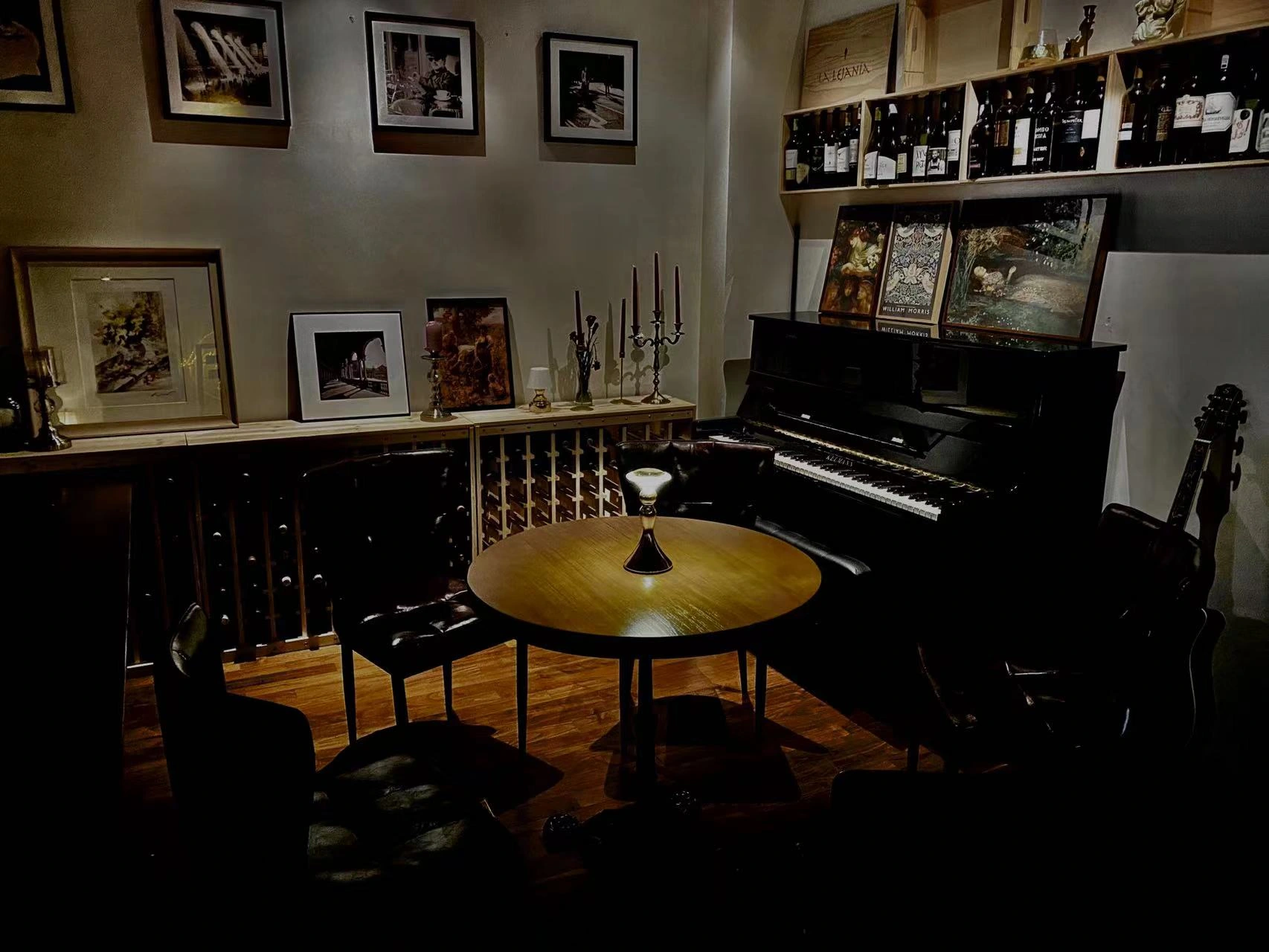 A piano and a lamplit table surrounded by photographs and wine